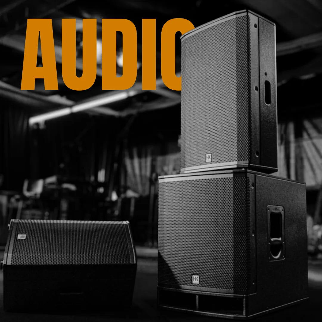 Professional black PA speakers and subwoofers arranged on a dark stage with bold orange audio text overlay.