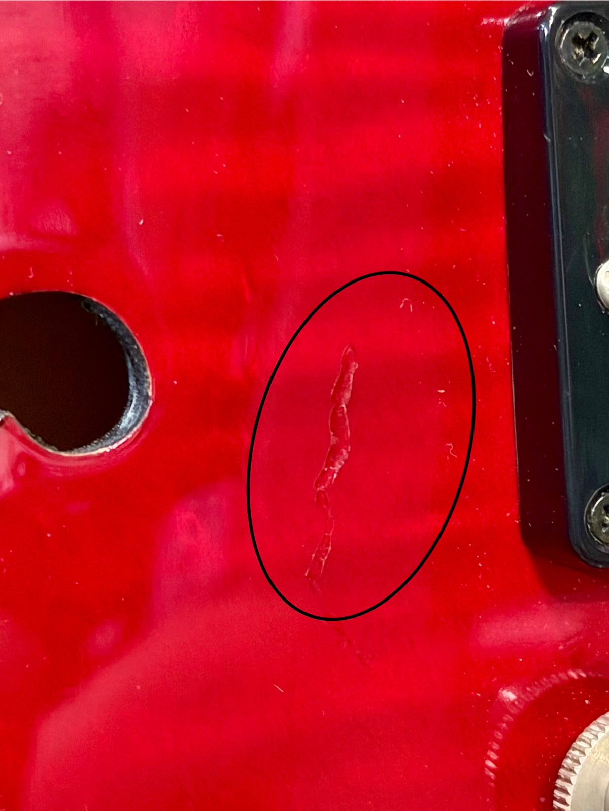 Close-up of a thin finish crack near the tailpiece mount on the body, circled to highlight the flaw.