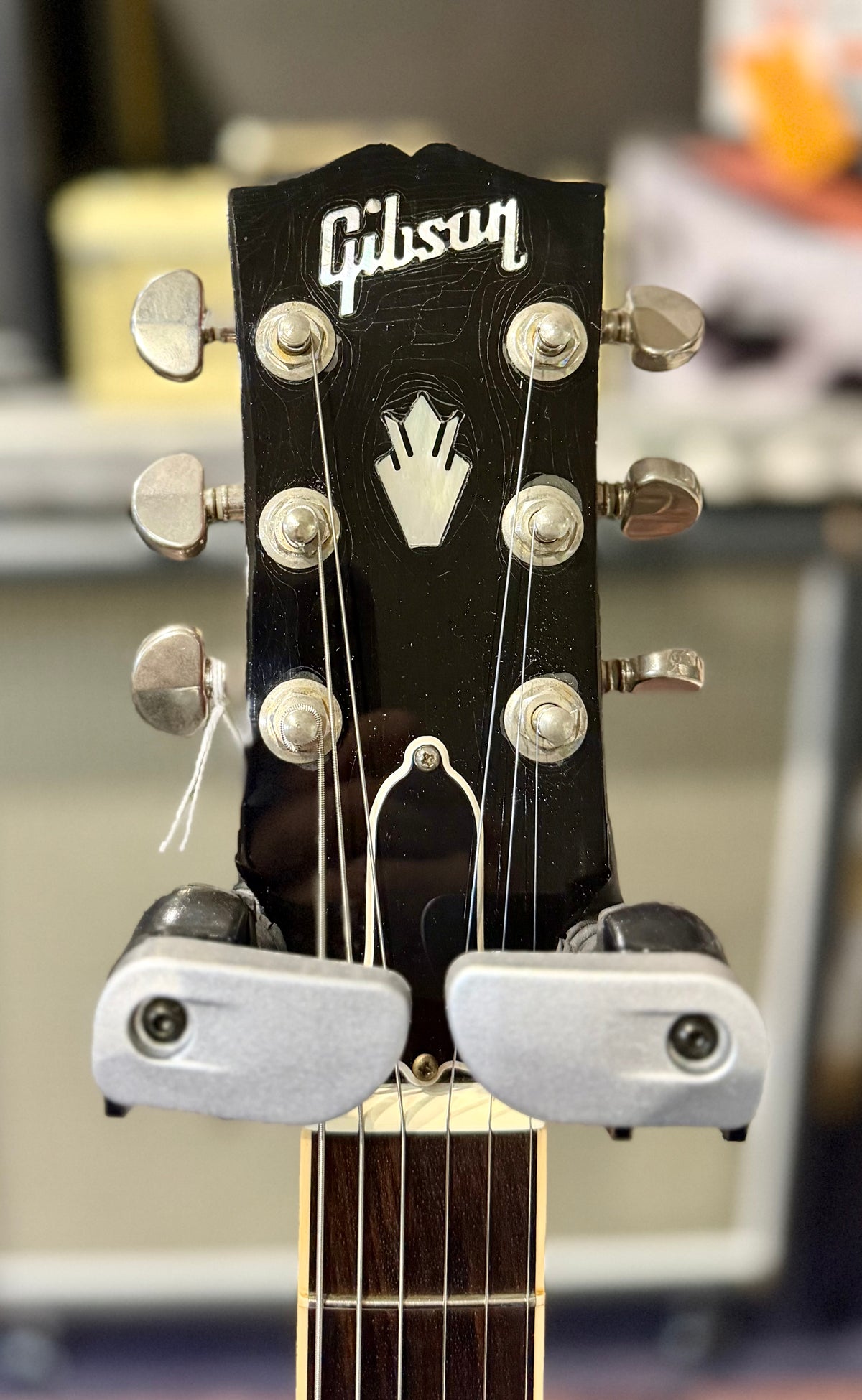 Front view of the black headstock with pearloid Gibson logo and crown inlay, Kluson-style tuners, and a locking clamp resting behind the nut.