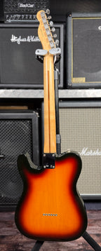Full-length rear view of the guitar on its stand, showing the maple neck, headstock back and body sunburst finish in front of amp stacks.