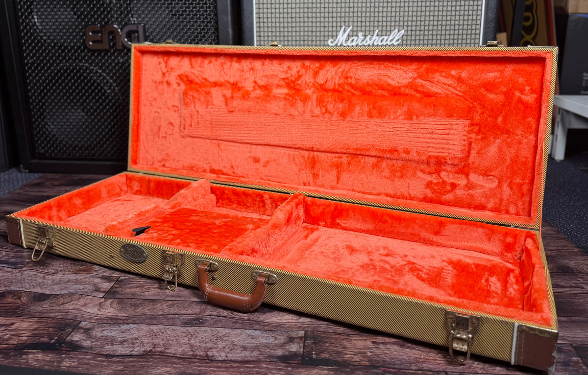 The tweed case shown open and empty, revealing its bright orange plush lining and Fender oval logo badge.