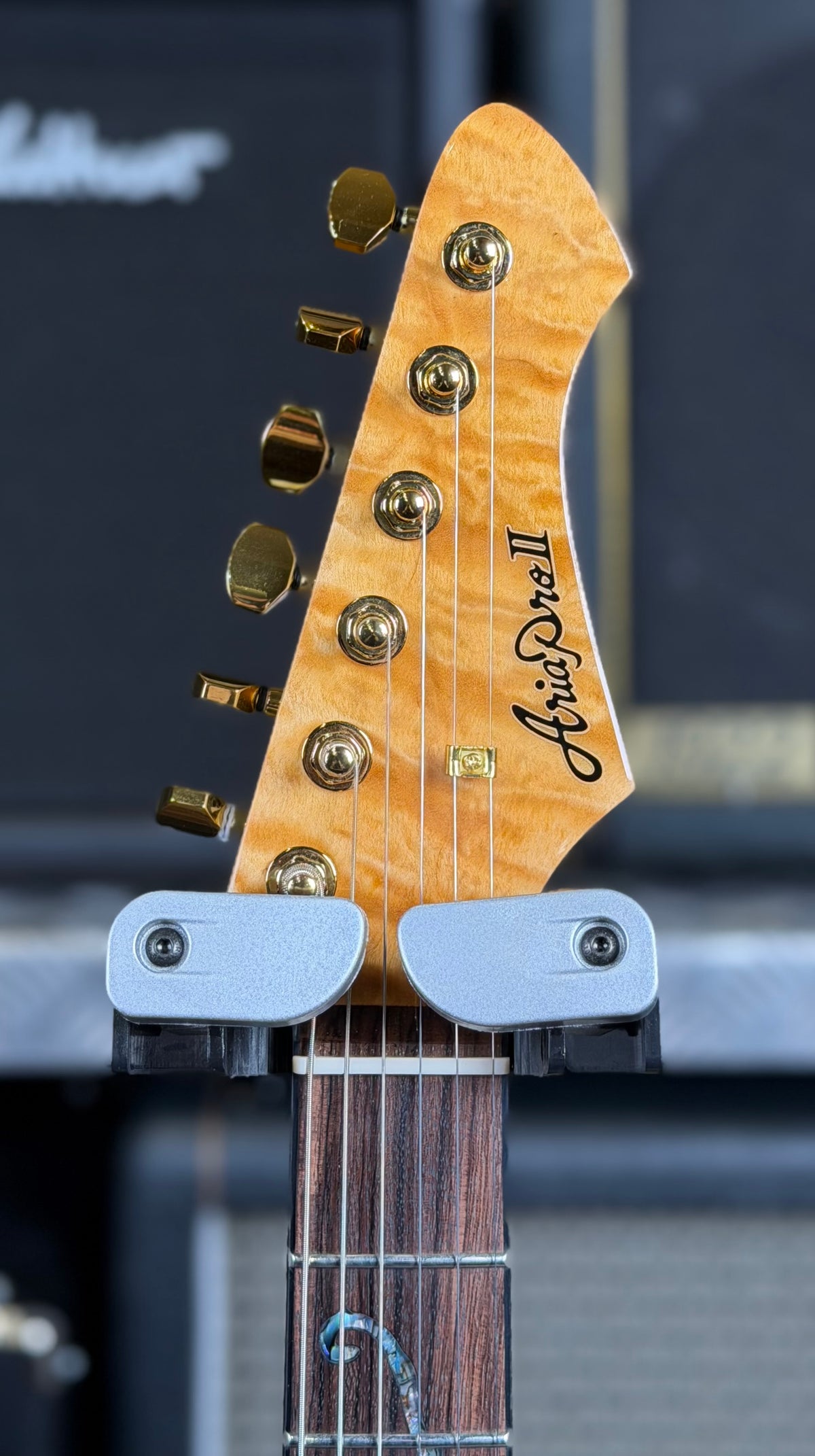 Close-up of the offset headstock showing the Aria Pro II logo, matching quilted maple veneer and gold tuners.