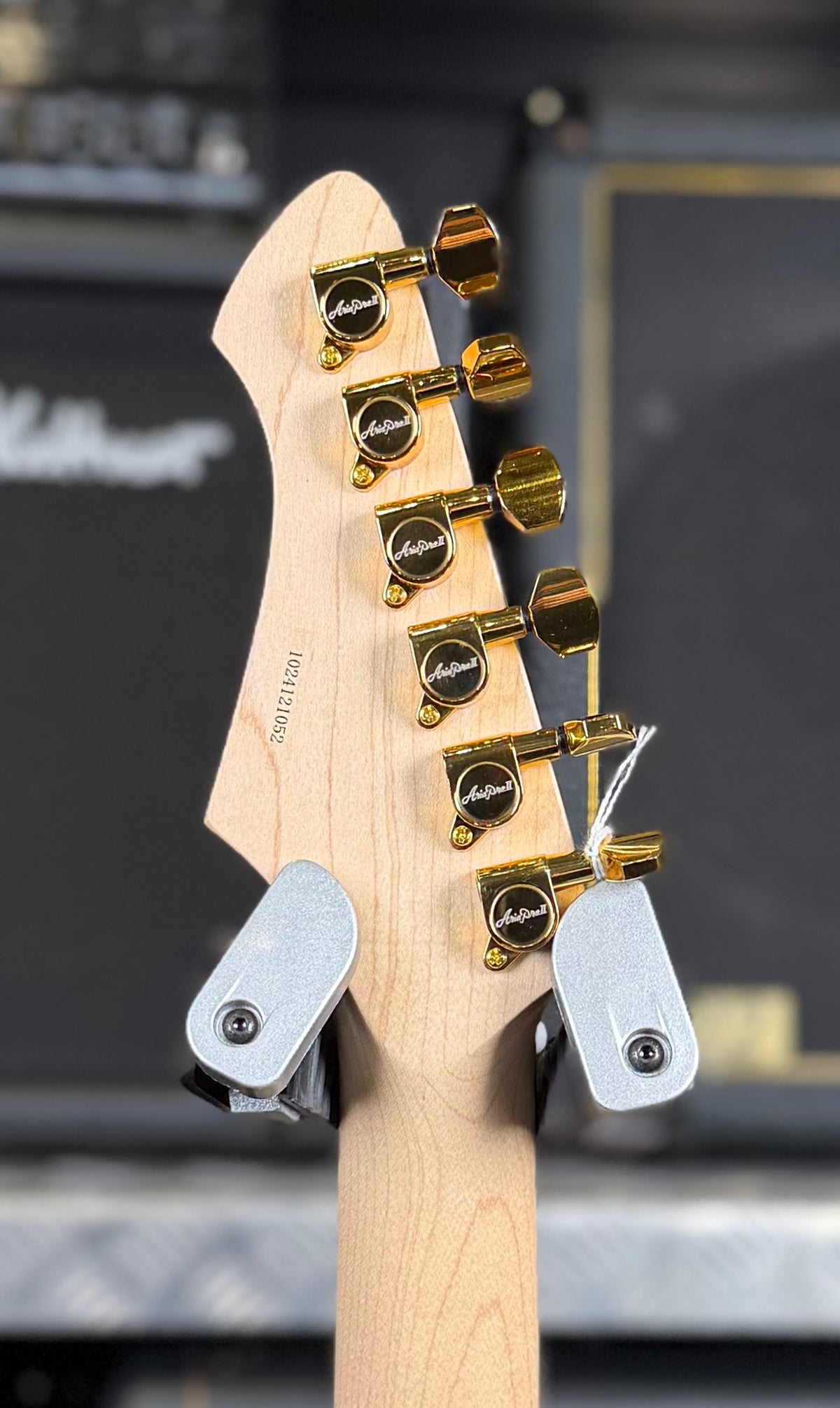 Close-up of the back of the headstock showing the maple neck, printed serial number and gold-plated locking tuners.
