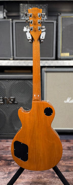 Full-length rear view showing the mahogany neck, headstock back and body on the stand in front of amp stacks.