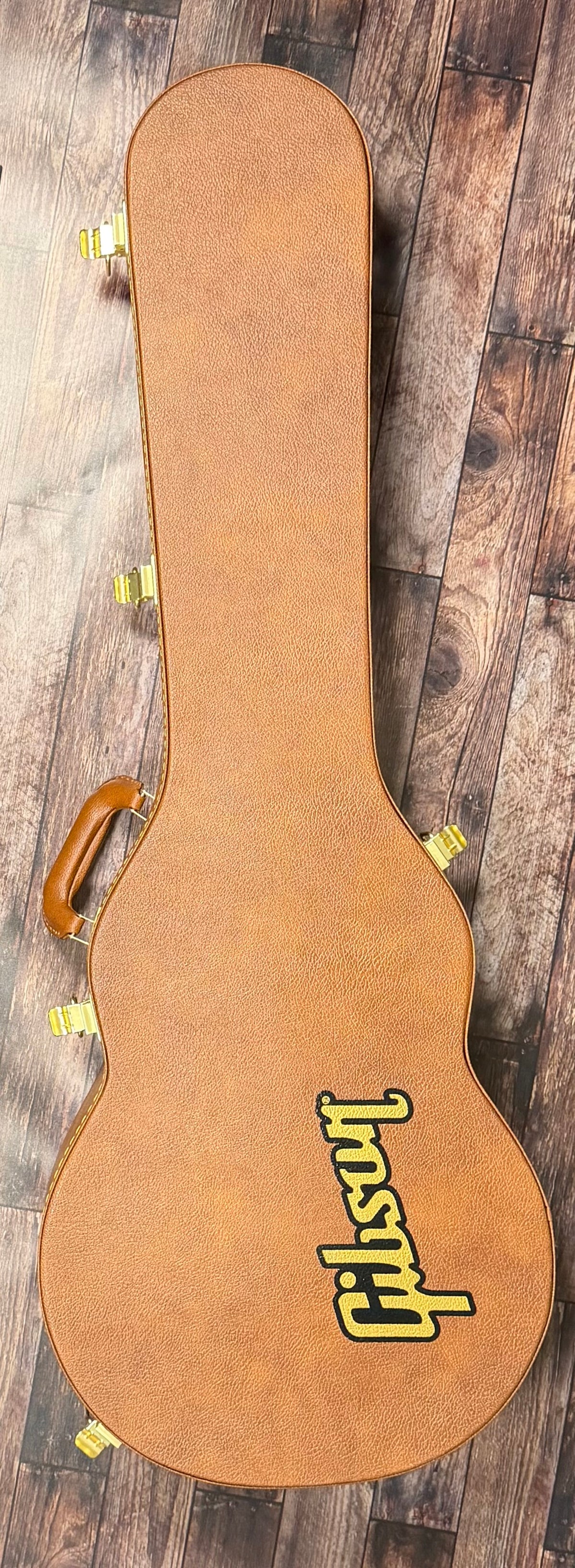The included tan Gibson hardshell case, shown closed with its yellow Gibson logo and leather handle.