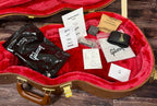 The case open showing the red plush lining, owner's manual, hang tags, polish cloth, Gibson strap, allen keys and desiccant bag, with the factory pre-pack checklist confirming the matching model and serial number.