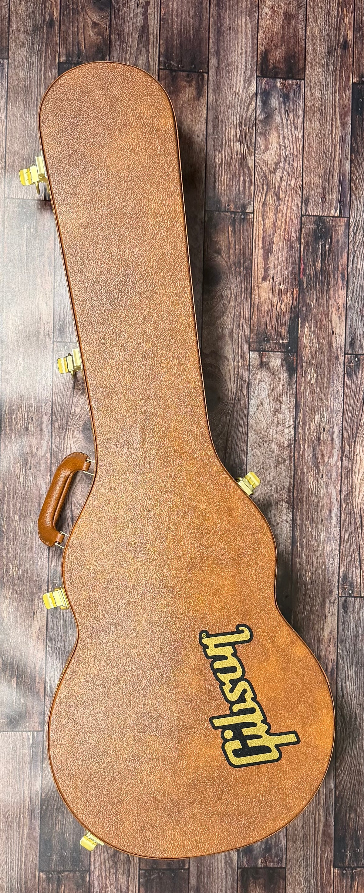The included tan Gibson hardshell case, shown closed with its yellow Gibson logo and leather handle.