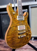 Three-quarter angled view showing the carved flame top and mahogany body edge, with the PRS bird inlays and toggle switch visible.