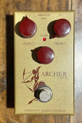 Front view of the J Rockett Audio Designs Archer Ikon pedal in its gold casing with burgundy knobs, showing the archer graphic and Output/Treble controls.
