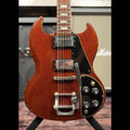 1971 Gibson SG Deluxe electric guitar in faded cherry finish, front view of the body and upper neck showing the two black-covered humbucker pickups, Maestro-style vibrato tailpiece and black control plate with four knobs and a toggle switch, photographed on a guitar stand in front of an amplifier.