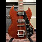 1971 Gibson SG Deluxe electric guitar in faded cherry finish, front view of the body and upper neck showing the two black-covered humbucker pickups, Maestro-style vibrato tailpiece and black control plate with four knobs and a toggle switch, photographed on a guitar stand in front of an amplifier.