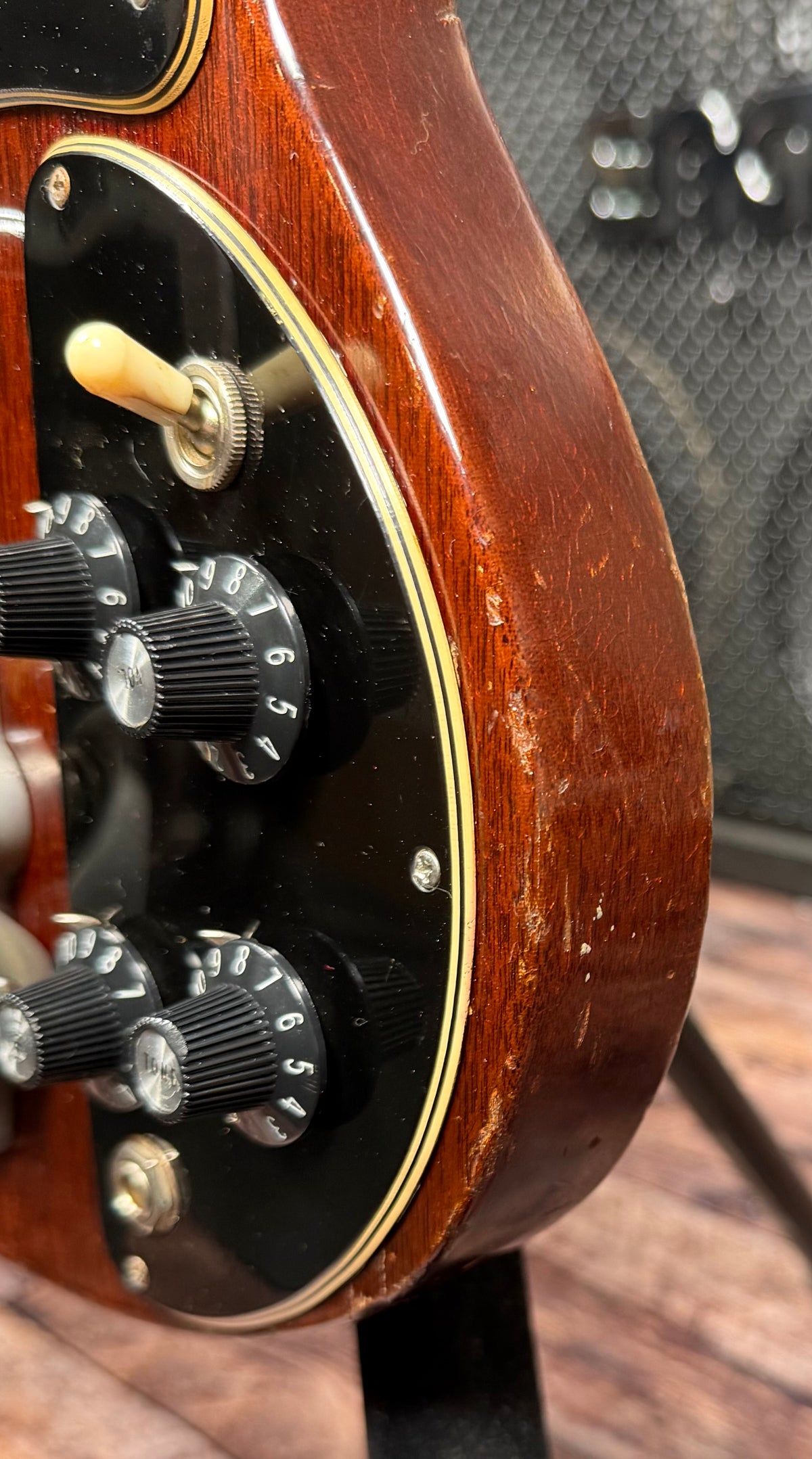 Close-up of the lower body edge of the Gibson SG Deluxe showing the control cavity with four knobs and the toggle switch, with visible finish wear along the edge.