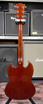 Full back view of the Gibson SG Deluxe from the headstock down the neck to the body, showing the faded cherry finish on the reverse of the instrument, in front of stacked amplifiers.