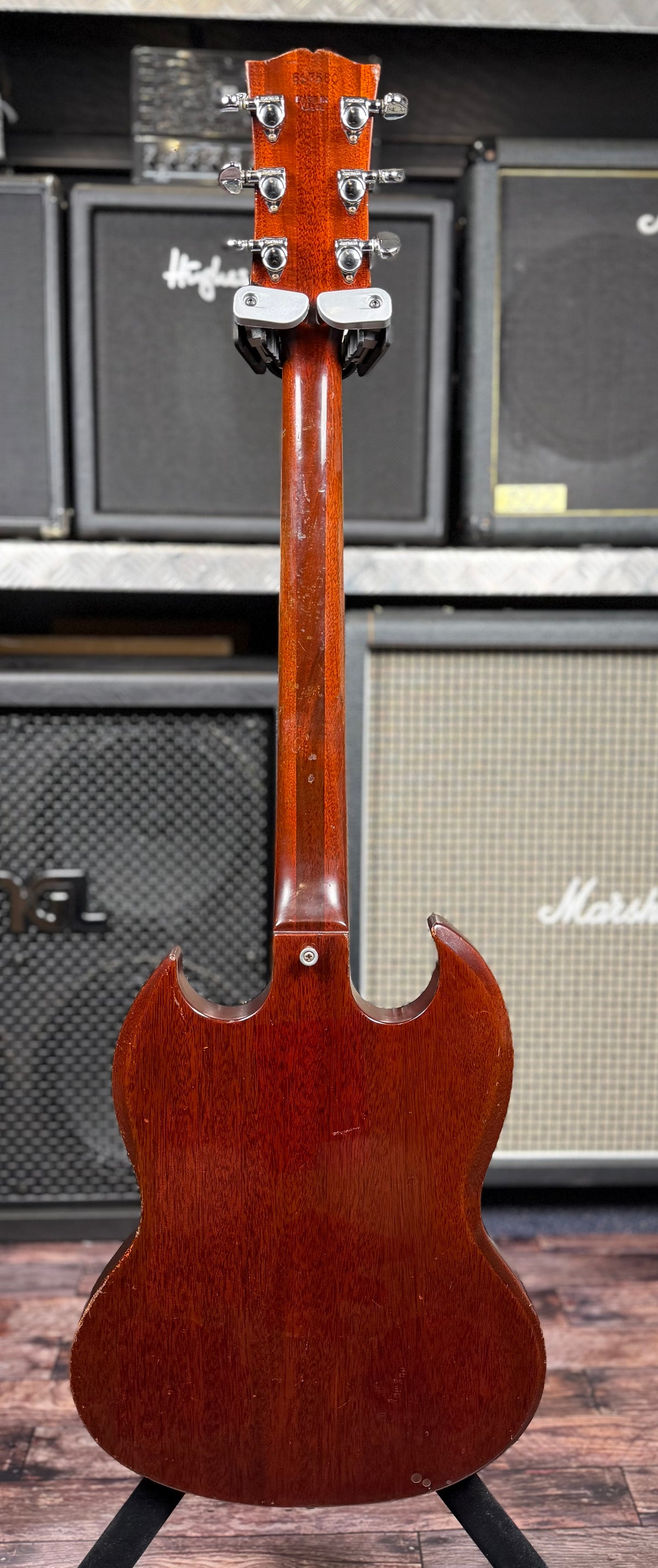 Full back view of the Gibson SG Deluxe from the headstock down the neck to the body, showing the faded cherry finish on the reverse of the instrument, in front of stacked amplifiers.