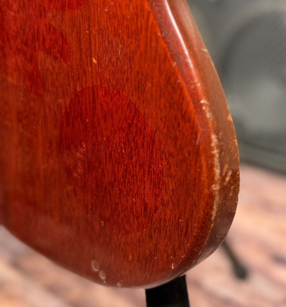 Close-up of the lower body edge of the Gibson SG Deluxe showing finish chipping along the curve, exposing the wood underneath.