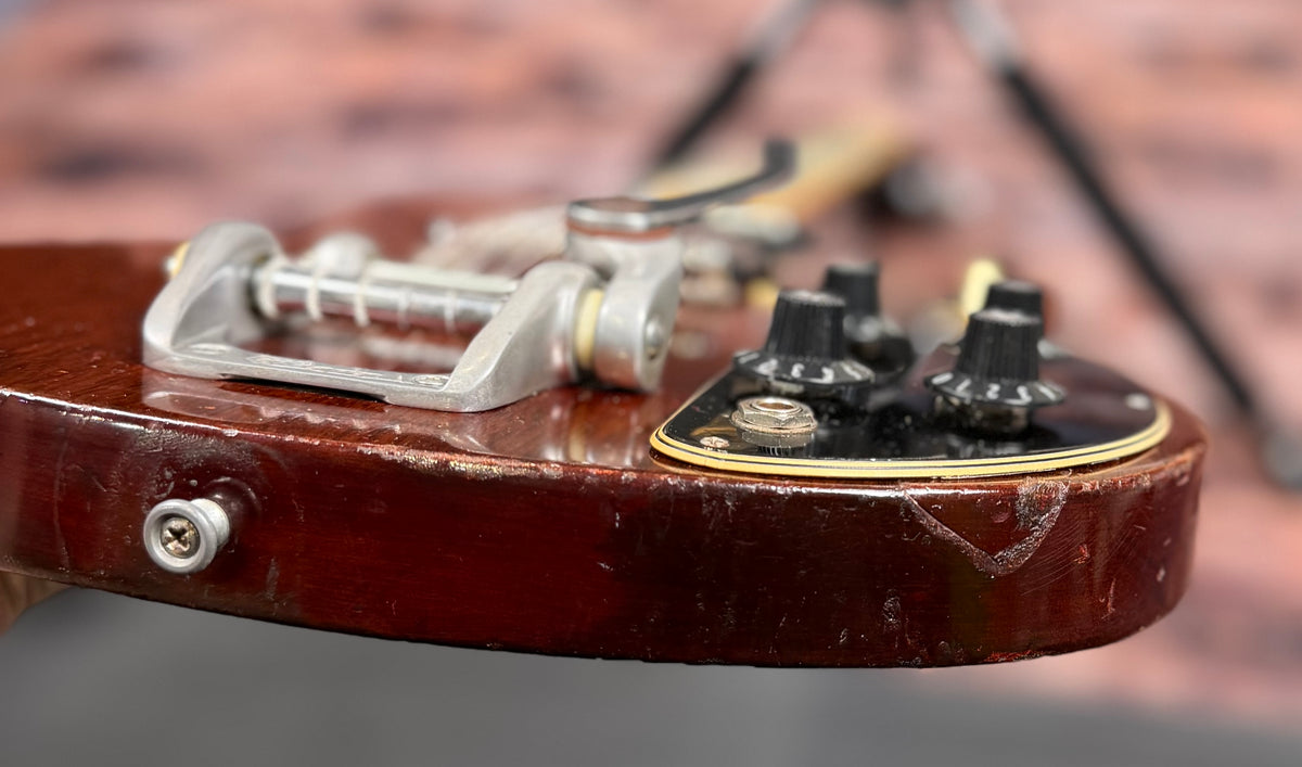 Close-up of the bottom edge of the Gibson SG Deluxe body showing the vibrato tailpiece, strap button, two control knobs and a visible chip in the finish.