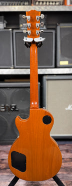Full-length rear view showing the neck, headstock back and mahogany body on the stand, with amp stacks in the background.