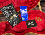Close-up of the case accessory pocket showing the polish cloth bag, Gibson Gold Warranty booklet, owner's manual and four spare gold control knobs.
