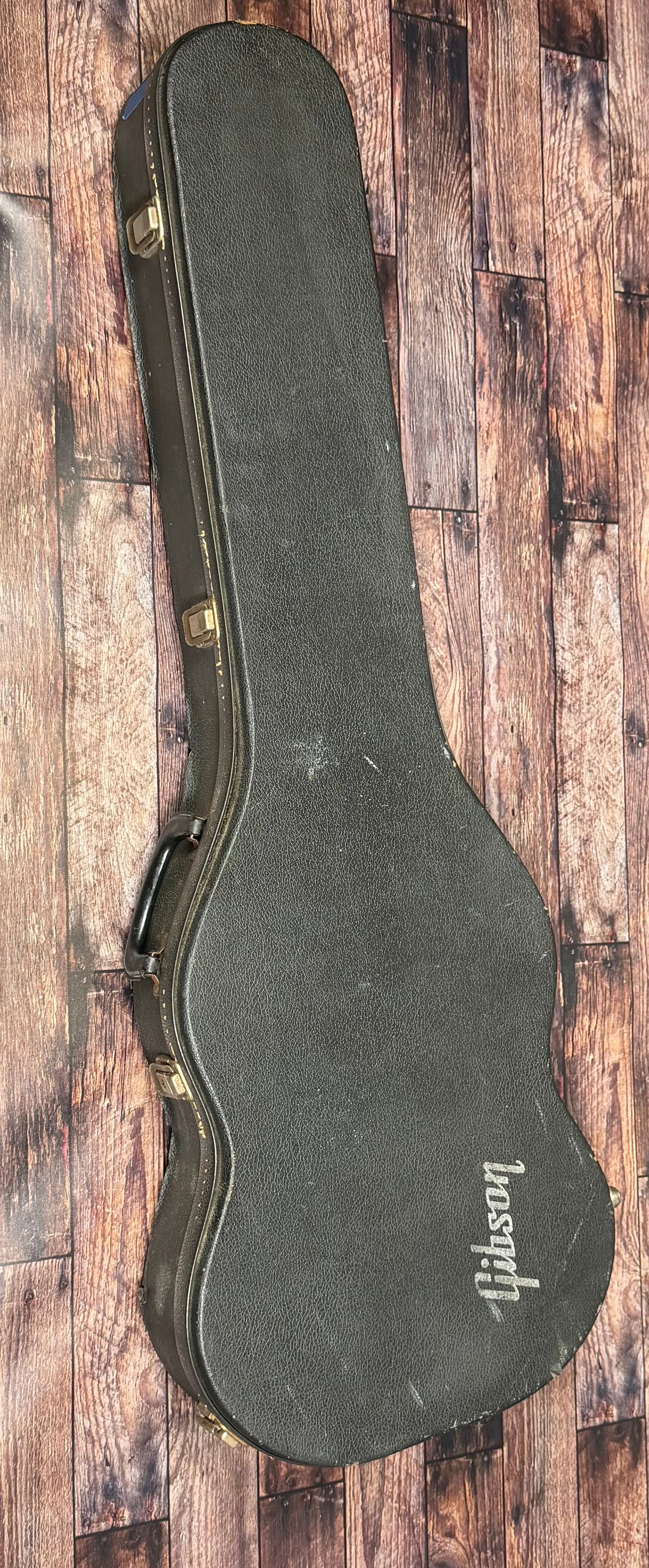 Closed black Gibson hardshell case for the SG Deluxe, viewed from above and resting on a wooden floor.