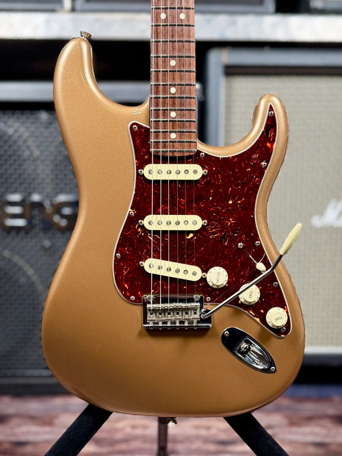 Front view of the Firemist Gold Stratocaster body on a guitar stand, showing the tortoiseshell pickguard, three single-coil pickups, control knobs and synchronised tremolo bridge.